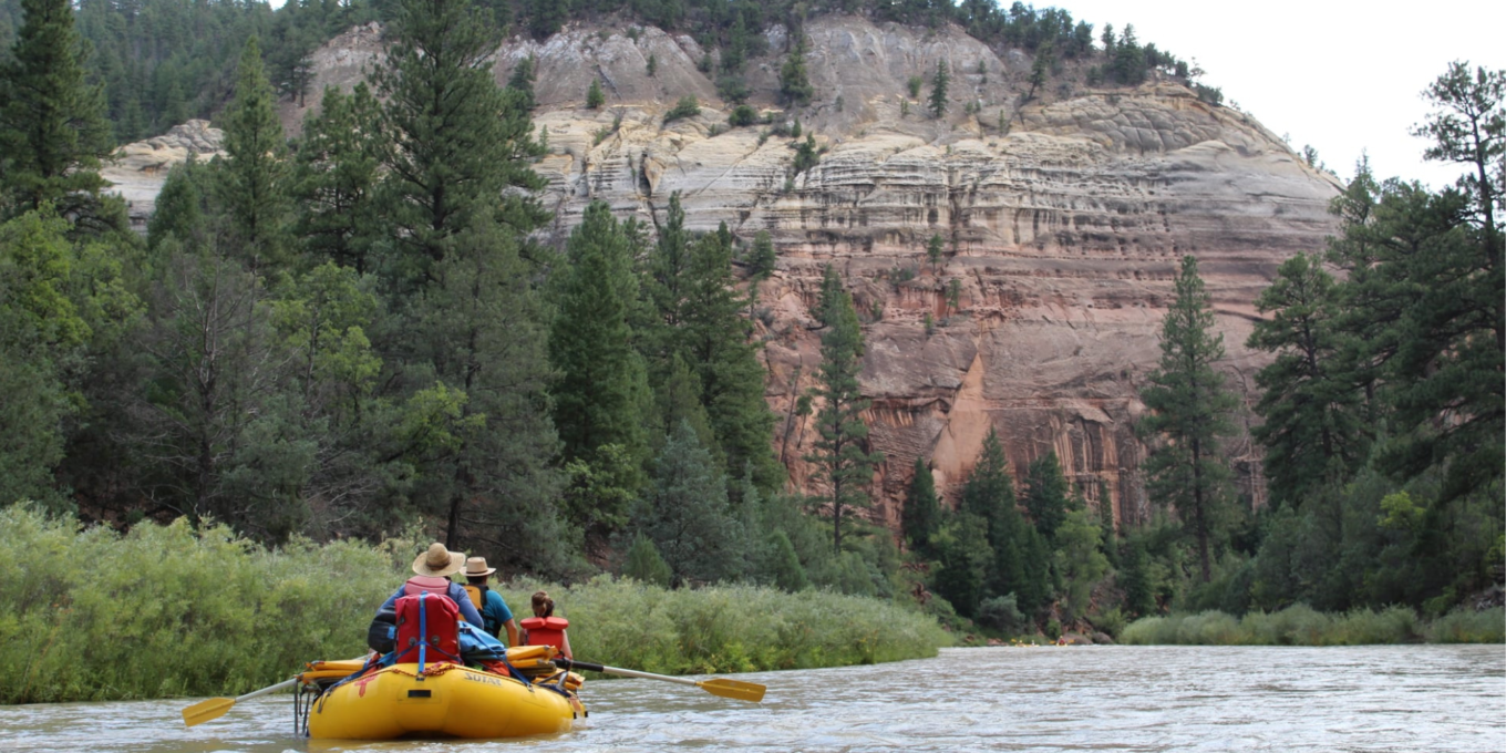 a yellow raft with three passengers floats down the river