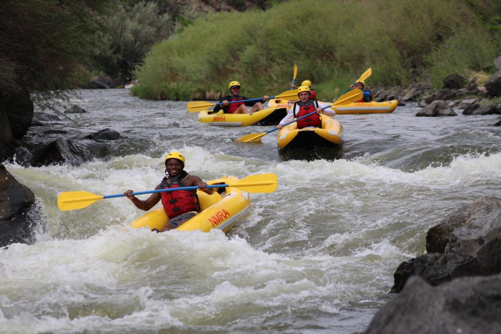people paddling in yellow inflatable kayaks down rapids while rafting the rio grande